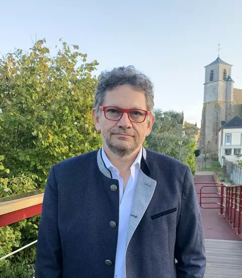 L'image montre un homme de face avec des lunettes noires et un costume rayé gris